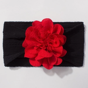 Détail d'un bandeau bébé en nylon noir avec une grande fleur rouge en mousseline douce
