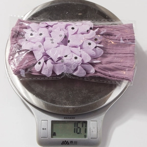 Purple nylon stretch baby headband with 3D floral petals being weighed at 16.7g on scale