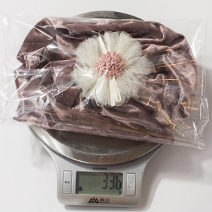 Close-up of brown velvet baby hat with white mesh flower on a digital scale weighing 33.6g