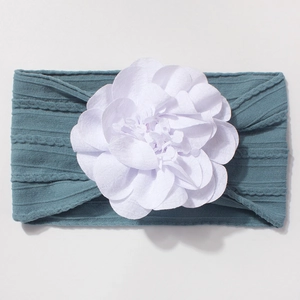 Détail du bandeau bébé en tricot côtelé bleu brume avec une grande fleur en tissu blanc