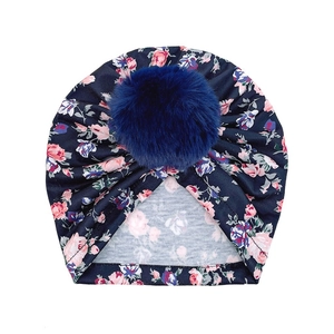Détail d'un bonnet turban pour bébé à imprimé fleuri et pompon en fausse fourrure bleu marine