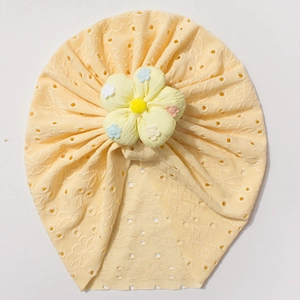 Detail of baby turban hat featuring a pale yellow hollow knit and a large floral accent