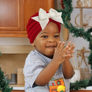 Bébé portant un bonnet en tricot rouge festif avec un grand nœud blanc de Noël