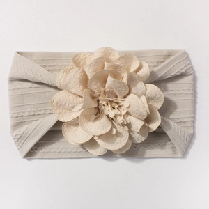 Détail du bandeau bébé en nylon beige avec texture torsadée et grande fleur en tissu doux