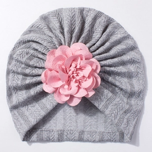 Détail d'un turban gris pour bébé avec une grande fleur rose en tissu doux