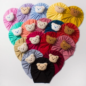 Variety of colorful baby beanies with teddy bear icons arranged in a large heart shape