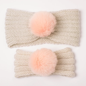 Close-up of mother and child cable knit headbands with soft faux fur pom-poms in off-white