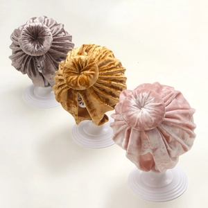 Three velvet baby donut hats in mauve, yellow and pink on white stands for winter comfort
