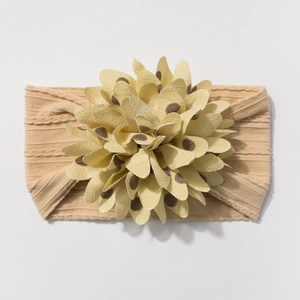 Close-up of beige knitted baby headband featuring a large polka dot fabric flower detail