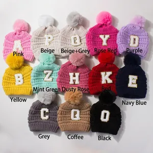Flat lay of knit beanies in 13 colors featuring large faux fur pom-poms and letter patches