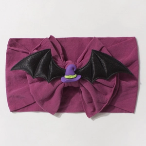 Detail of purple knitted baby headband featuring black bat wings and mini wizard hat