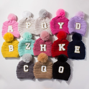 Knitted baby hats with faux fur pom poms and sequined letter patches in multiple colors