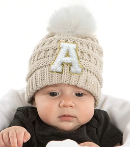 Close-up of knit baby beanie in beige with fluffy white pompom and letter A patch