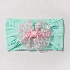 Détail du bandeau bébé vert menthe avec un nœud en dentelle rose brodée fleurie