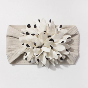 Detailed view of beige knit baby headband with 3D white black polka dot flower accessory
