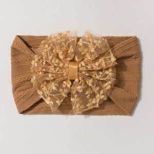 Détail d'un bandeau bébé en maille torsadée avec grand nœud floral en tulle marron chaud