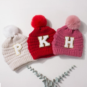 Winter knitted baby hats in beige, red and pink with fluffy pom-poms and letter patches