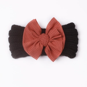 Detail eines schwarzen Strick-Stirnbands für Babys mit großer rostrot gerippter Schleife