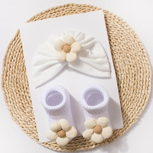 Close-up of white knit baby hat and socks set featuring large beige corduroy flowers