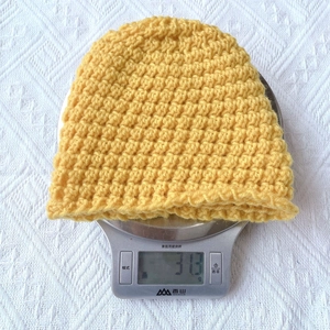 Macro shot of yellow thick knit baby hat weighing 31.3g on an electronic scale for warm comfort