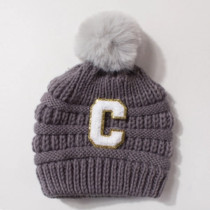 Close-up of baby knit beanie with fluffy pom-pom and gold sequined letter C patch