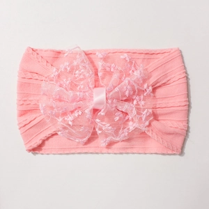 Détail d'un bandeau rose nervuré pour bébé avec un grand nœud en dentelle délicat