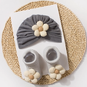 Detail of baby knit hat and socks set with 3D beige flowers on a woven mat background
