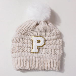 Detailed close-up of beige knit baby hat with white pompom and sparkling letter P patch