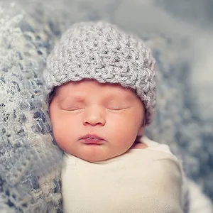Close-up of light grey hand-knitted baby hat with wave texture and white wrap