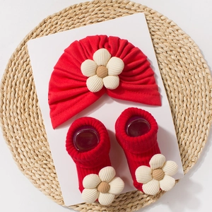 Detailed view of baby red turban hat and socks set with beige fabric flower accents