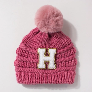 Close-up of knit baby hat featuring pink pom-pom and gold-bordered H letter embroidery