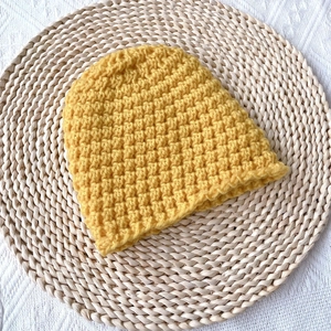Thick ginger knit baby beanie with textured honeycomb pattern on rustic straw mat background