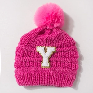 Close-up of knit baby hat with pink faux fur pom-pom and embroidered letter Y patch