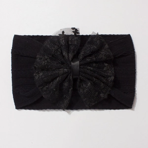 Détail d'un bandeau bébé en nylon jacquard noir avec un grand nœud en dentelle et tissu côtelé
