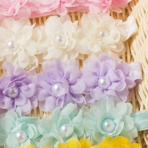 Détail de bandeaux bébé avec fleurs en mousseline et perles en couleurs pastel sur osier
