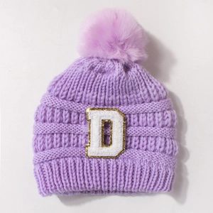 Detail of purple knit baby hat featuring fuzzy pom pom and sparkly chenille letter D