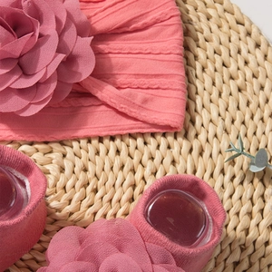 Detail of pink baby headband and socks set with 3D flower petals on a straw mat