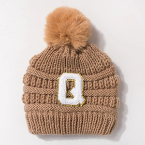 Detail of baby knit hat with cable pattern, faux fur pom-pom and letter Q patch