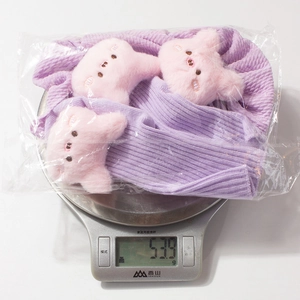 Detail view of purple knitted baby accessory with pink plush animal decor on a scale