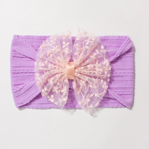 Détail d'un bandeau bébé en nylon avec grand nœud en dentelle rose et texture violette côtelée