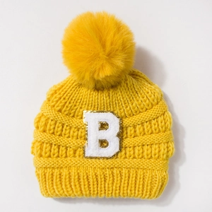 Detail of yellow knit beanie featuring a large pompom and a sequined letter B patch