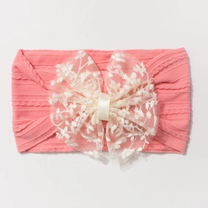 Détail d'un bandeau rose pour bébé avec un nœud en dentelle blanche brodée délicat