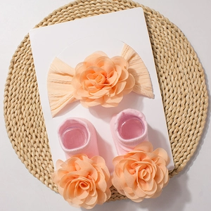 Detail of baby headband and socks set featuring 3D floral accents on a textured background