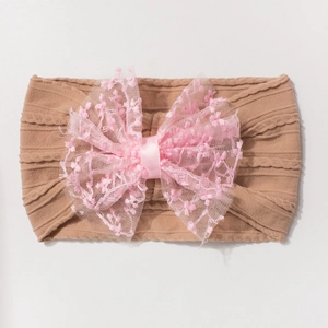 Détail d'un bandeau bébé avec un grand nœud en dentelle rose et broderie florale fine