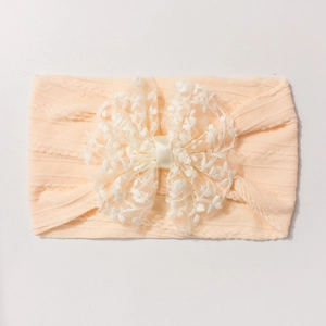 Vue à plat d'un bandeau élastique pour bébé pêche avec un nœud en dentelle blanche