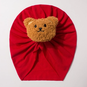 Red pleated baby turban hat featuring a cute brown plush bear icon on a soft knit fabric