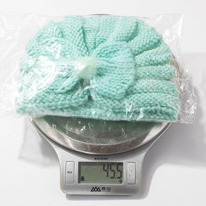 Detail showing mint green baby knit hat with bow weighing 45.5g on a scale