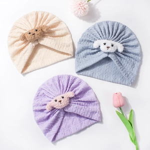 Detail of ribbed knit baby turban hats with cute plush puppy embellishment in soft colors