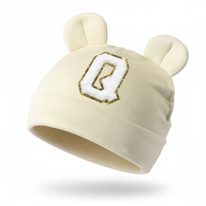 Close-up of baby beanie with plush ears and golden glitter letter Q patch on soft knit