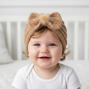 Detail of baby turban knit hat in khaki with a large bow and soft faux fur pom-pom